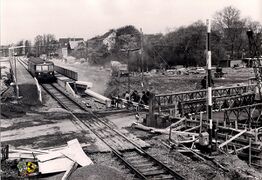 Bild 2: Blick vom Stellwerk Hrb des Bahnhofs Herne-Rottbruch nach Nordosten. Ein Personenzug Richtung Bochum steht auf der neuen Brücke (zugleich Haltepunkt Herne-Rottbruch), die später über die Autobahn (heute A 43) führen wird. Die Ausschachtungsarbeiten für die Autobahn, die hier bekanntlich in einem Einschnitt verläuft, sind in vollem Gange. Im Vordergrund der Bahnübergang Rottbruchstraße, die Straße mündet rechts in den Grenzweg. Die Behelfsbrücke rechts steht ebenfalls im Zusammenhang mit den Ausschachtungsarbeiten.